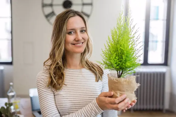 Portrait of smiling woman holding plant at home
