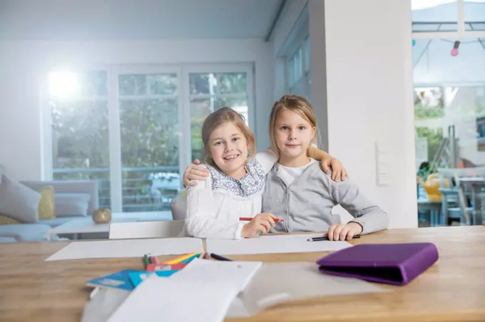 Portrait of two girls embracing doing homework at table together