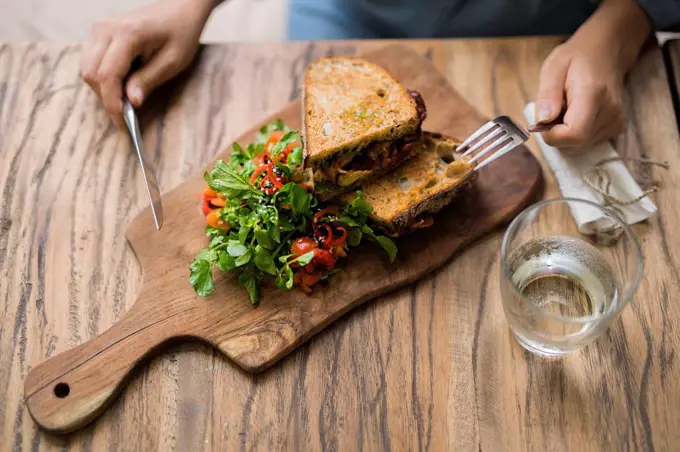 Hands holding knife and fork at wooden table with decorated salad and crusty bread