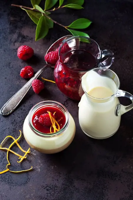 Glass of pudding with vanilla sauce and raspberry sauce garnished with raspberry and orange zest