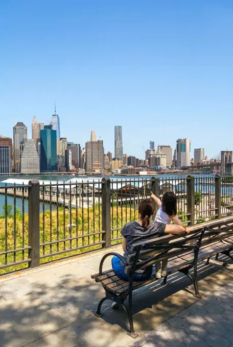 USA, New York, Brooklyn, Back view of woman and young girl sitting on bench while looking the skyline of Manhattan from Brooklyn