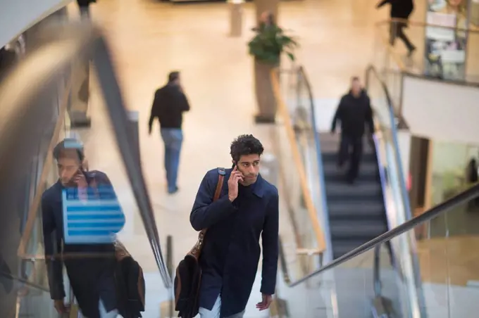 Man on the phone standing on escalator in a shopping mall