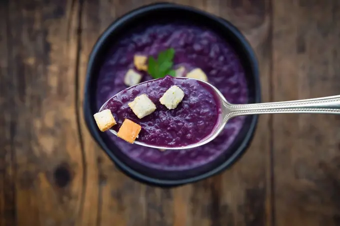 Red cabbage soup and croutons on spoon