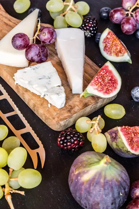 Plate with cheese, figs, grapes, blueberries, brambles, pecan, chopping board, knife