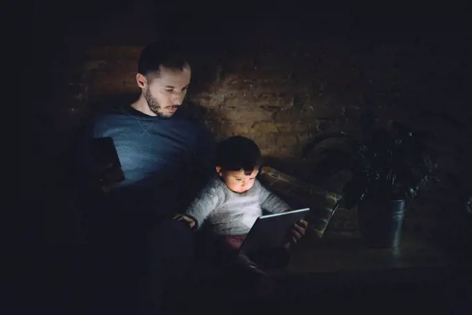 Father and daughter looking at digital tablet at home in the dark