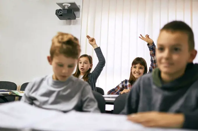 Students in class with two girls raising their hands