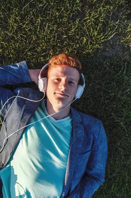 Portrait of redheaded young man with headphones lying on grass