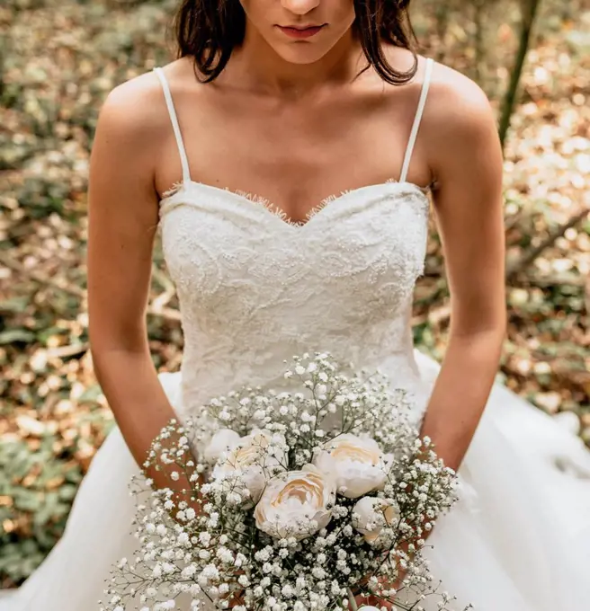 Close-up of bride holding bouquet of flowers in forest