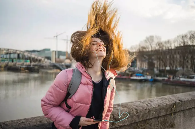 Paris, France, happy young woman listening music with earphones and smartphone tossing her hair