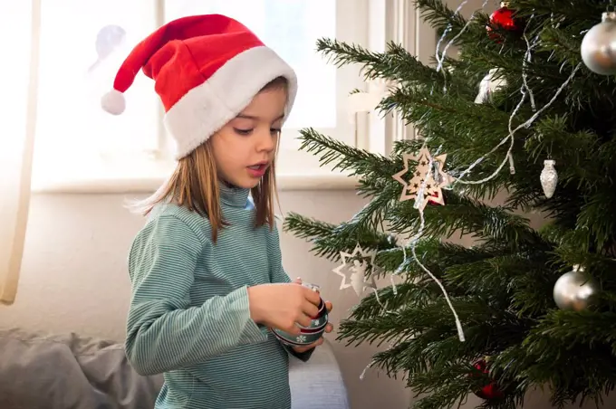 Little girl wearing Christmas cap decorating Christmas tree