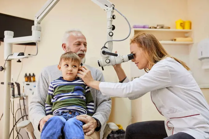 ENT physician examining ear of a boy sitting on grandfather's lap