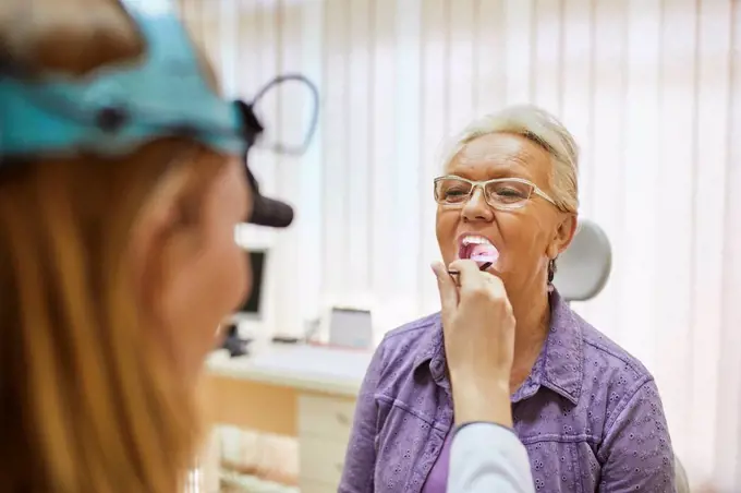 ENT physician examining mouth of a senior woman