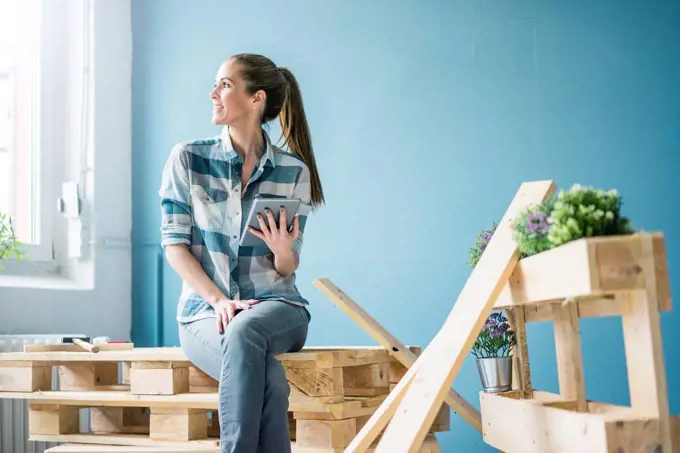Woman refurbishing her new home with pallets, holding digital tablet