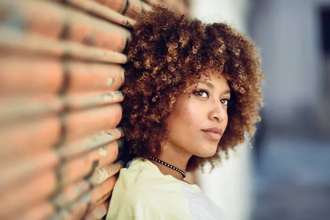 Portrait of woman with afro hairstyle leaning against roller shutter