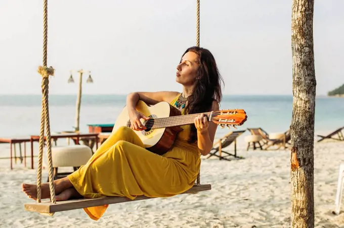 Thailand, Koh Phangan, woman playing guitar at the beach