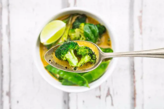 Green thai curry with broccoli, pak choi, snow peas, baby spinach, lime, broccoli and sauce on spoon