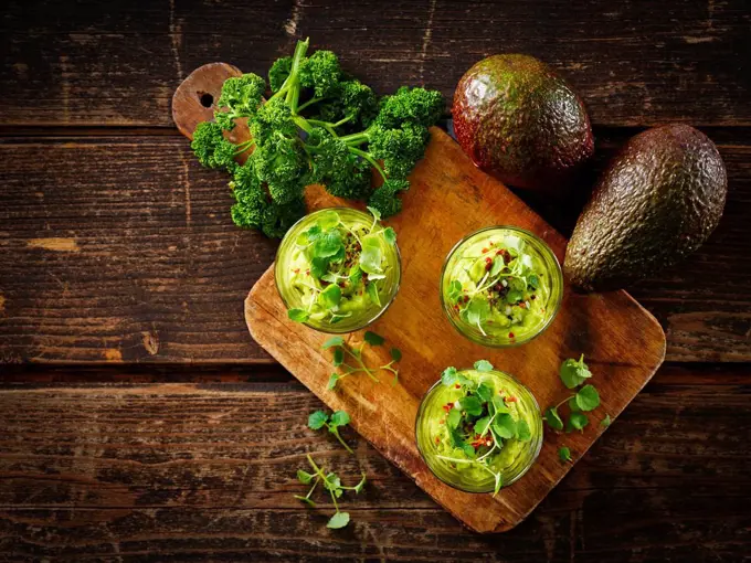 Glasses of avocado cream with chili flakes, cress and parsley