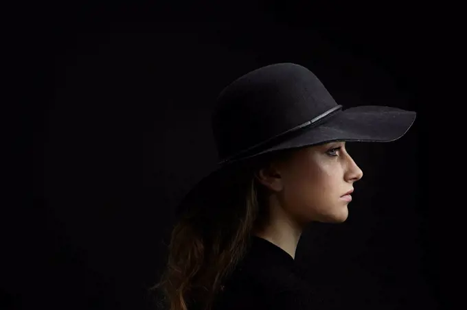 Profile of sad young woman wearing black hat against black background