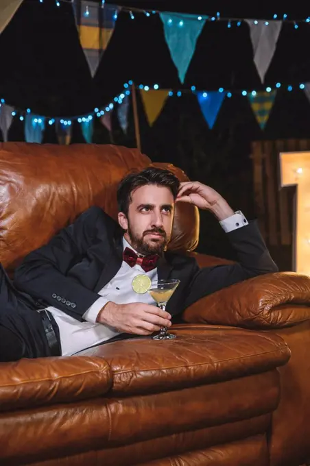 Pensive man in suit lying on sofa on a night party oitdoors