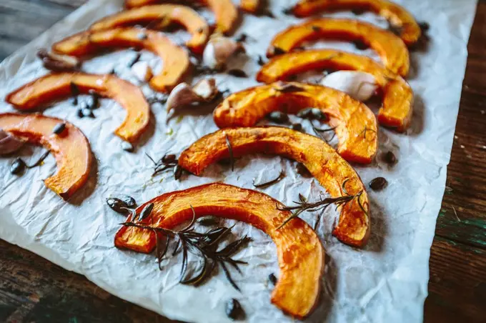Baked slices of pumpkin, garlic and rosemary on baking paper