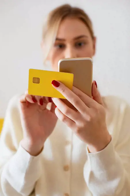 Blonde woman using smartphone and using bank card at home
