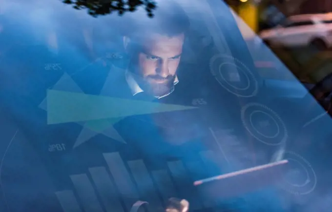 Businessman with tablet in car at night surrounded by data
