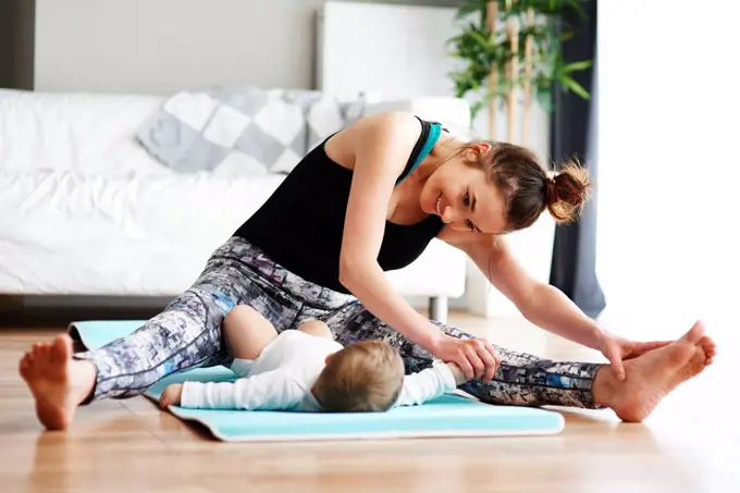 Mother with baby exercising on yoga mat at home