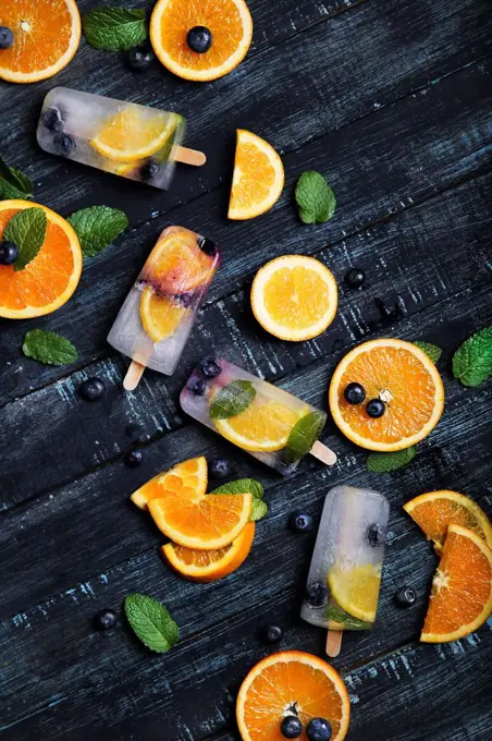 Homemade detox popsicles with blueberries, orange slices and mint leaves on black wood