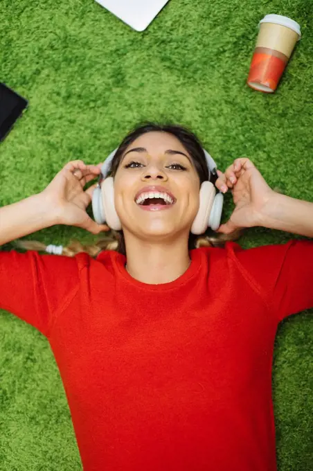 Happy young woman lying on carpet listening to music with headphones