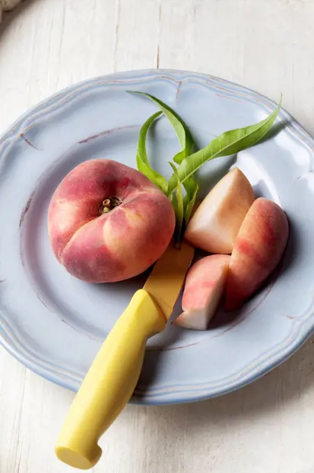 Vineyard peach (Prunus persica) and slices of vineyard peach on plate, studio shot