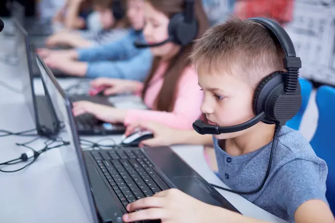 Pupils wearing headsets and using laptops in school