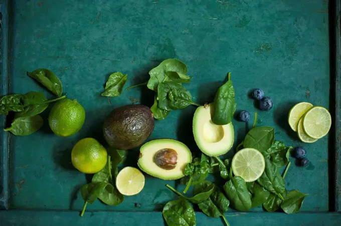 Spinach leaves, avocados and blueberries on green ground