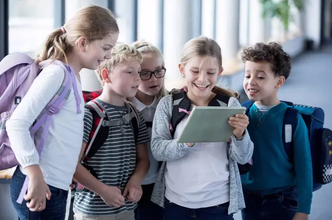 Happy pupils looking at tablet on school corridor