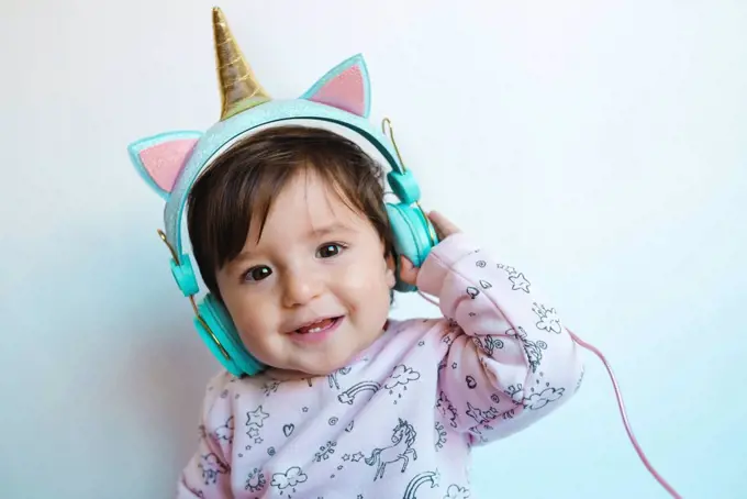 Portrait of smiling baby girl with unicorn headphones listening music