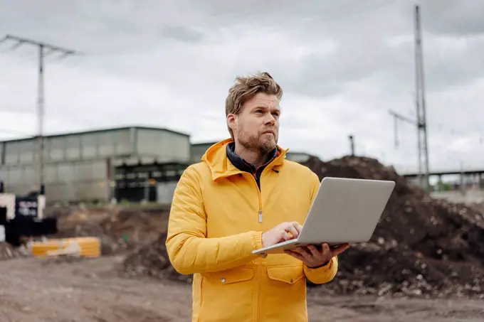 Man holding laptop, construction site in the background