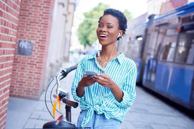 Portrait of laughing woman with earphones and cell phone in the city