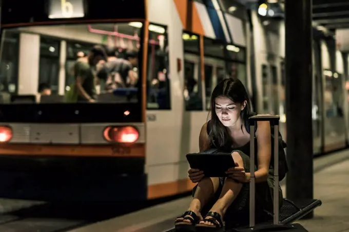 Portrait of young woman waiting at tram stop by night using tablet