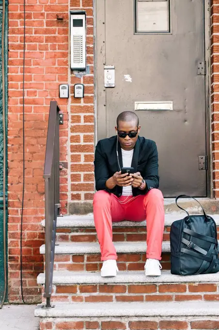 USA, NYC, Brooklyn, Man waiting on stairs, using smartphone