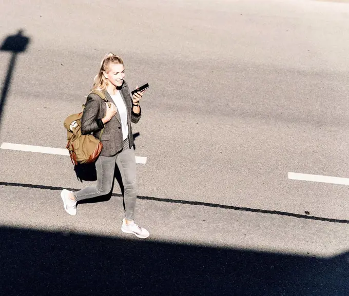 Young woman walking on empty road, talking into her smartphone