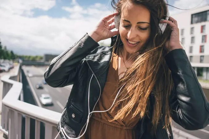 Smiling young woman listening to music on motorway bridge