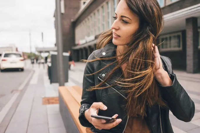 Young woman with windswept hair holding cell phone in the city