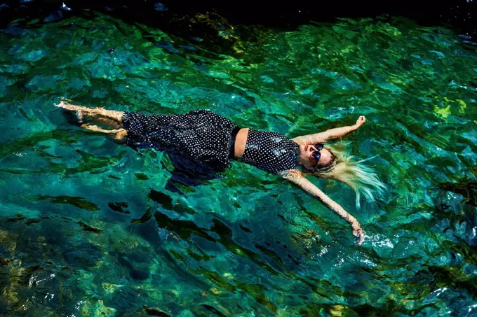 Young woman floating with dress on water in lagoon