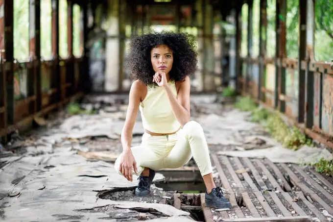 Portrait of fashionable young woman crouching in abandoned and destroyed old train