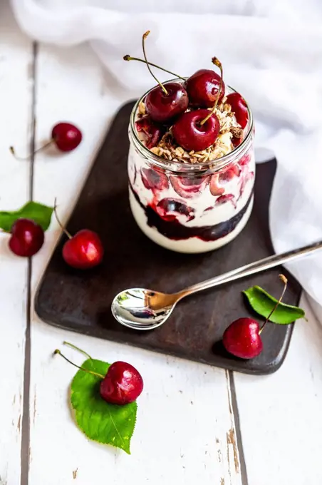 Glass of natural yoghurt with cherries, cherry jam and granola