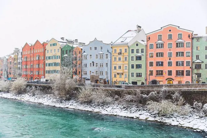 Austria, Innsbruck, row of colourful houses in winter with Inn River in the foreground