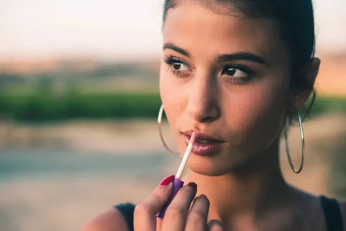 Portrait of teenage girl in nature applying lip gloss