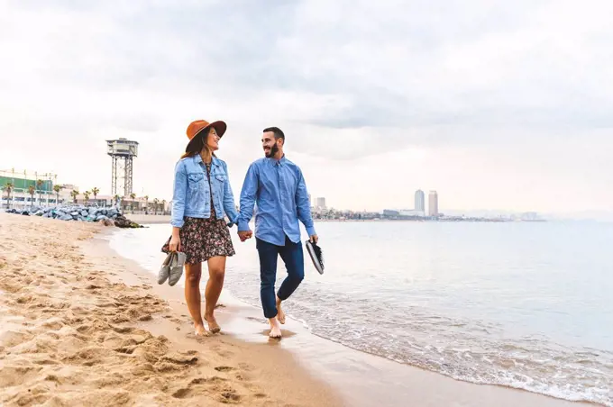 Spain, Barcelona, couple walking barefoot on the beach