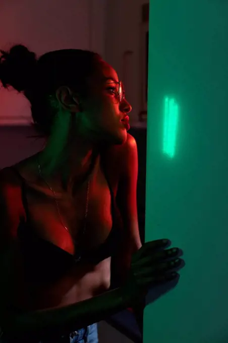 Portrait of beautiful young woman wearing bra and glasses in a dark illuminated room