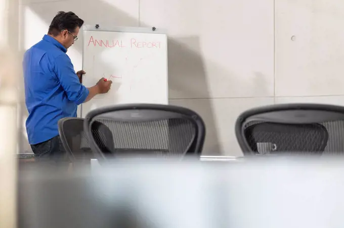 Businessman writing on whiteboard in conference room
