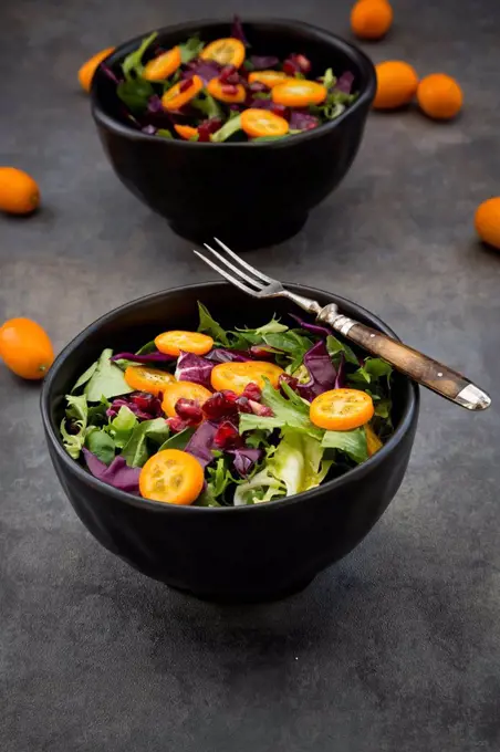 Bowl of mixed green salad with red cabbage, kumquat and pomegranate seeds